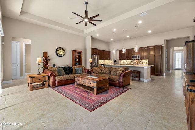 living room with a high ceiling, a raised ceiling, and ceiling fan