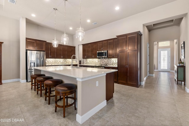 kitchen featuring sink, decorative light fixtures, a center island with sink, stainless steel appliances, and a high ceiling