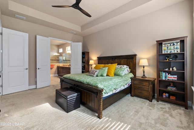 bedroom featuring light carpet, ensuite bath, a raised ceiling, and ceiling fan