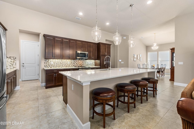 kitchen featuring pendant lighting, dark brown cabinetry, sink, and an island with sink