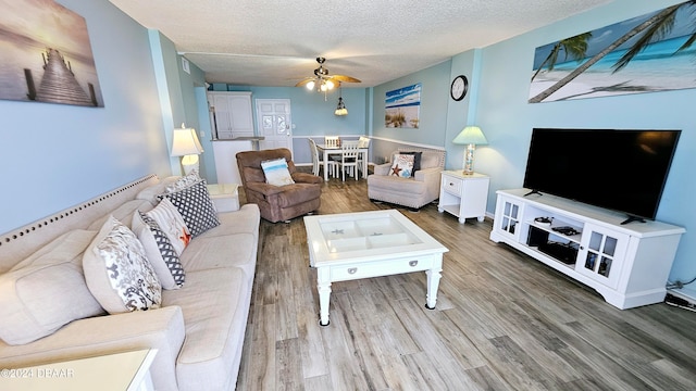 living room featuring wood-type flooring, a textured ceiling, and ceiling fan