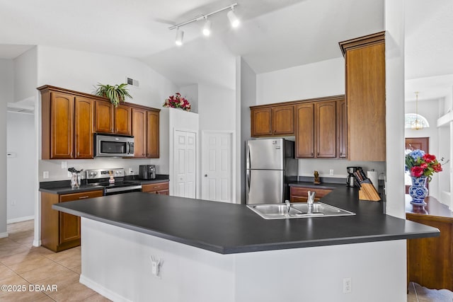 kitchen with light tile patterned floors, dark countertops, appliances with stainless steel finishes, a peninsula, and a sink