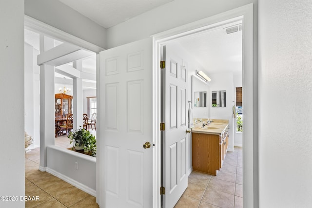 corridor with light tile patterned floors, visible vents, an inviting chandelier, a sink, and baseboards