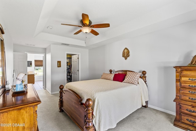 bedroom with a tray ceiling, light colored carpet, visible vents, and baseboards