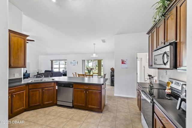 kitchen featuring light tile patterned floors, dark countertops, appliances with stainless steel finishes, a peninsula, and a sink