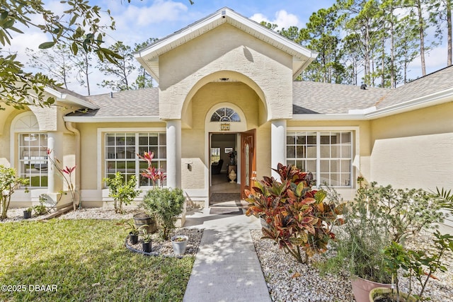 property entrance with a yard, a shingled roof, and stucco siding