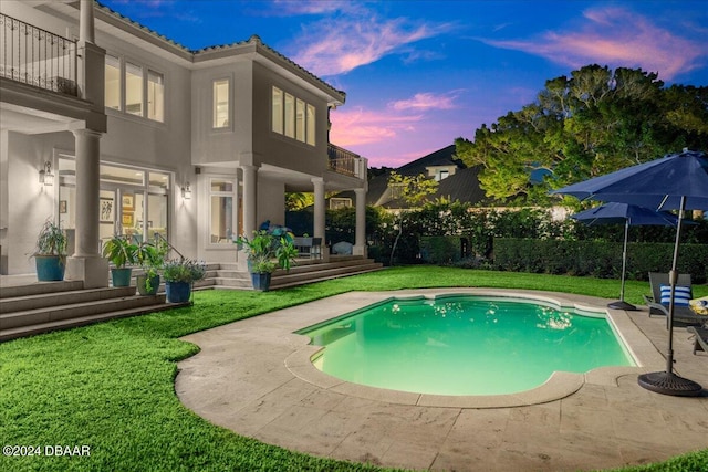 pool at dusk with a lawn and a patio