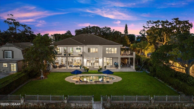 back house at dusk featuring a lawn, a balcony, and a patio area