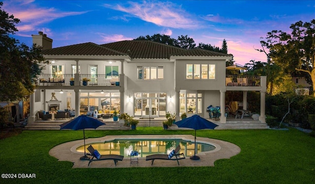 back house at dusk with a patio, a balcony, and a yard