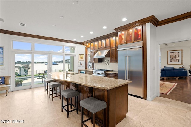 kitchen with high quality appliances, extractor fan, a kitchen island with sink, and crown molding