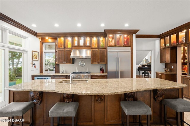 kitchen with a center island with sink, wall chimney range hood, crown molding, and stainless steel appliances