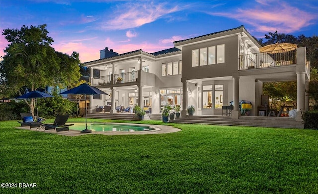 back house at dusk with a lawn, a balcony, and a patio area