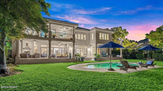 back house at dusk with an outdoor living space, a lawn, ceiling fan, and a balcony