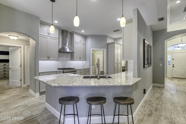 kitchen with light stone countertops, kitchen peninsula, gas range, sink, and wall chimney range hood