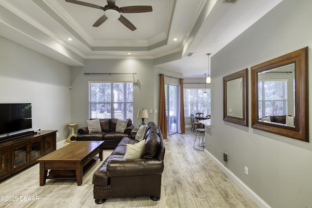 living room with a raised ceiling, ceiling fan, light hardwood / wood-style flooring, and a healthy amount of sunlight