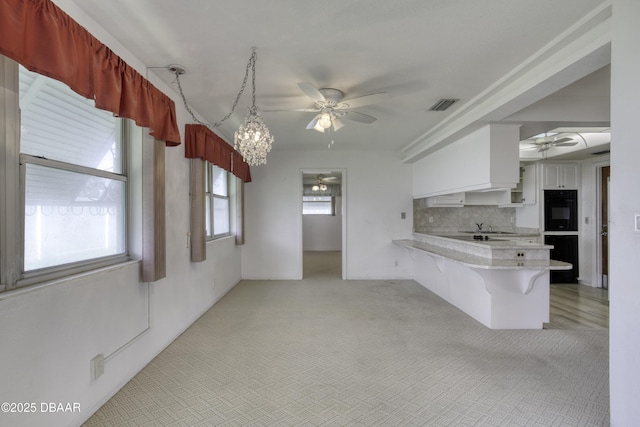 34 Kathy Dr, Ormond Beach, FL 32176 - kitchen with ceiling fan, a peninsula, a breakfast bar area, white cabinetry, and backsplash