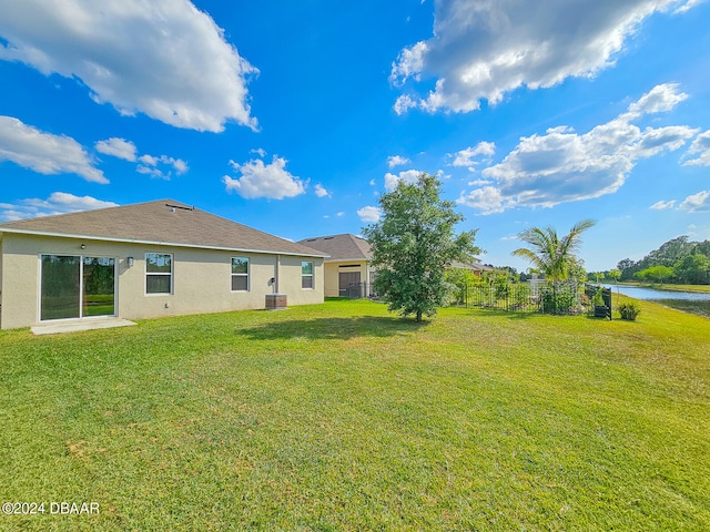 rear view of property featuring cooling unit, a water view, and a lawn