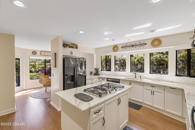 kitchen featuring stainless steel gas stovetop, white cabinets, a sink, light stone countertops, and black fridge