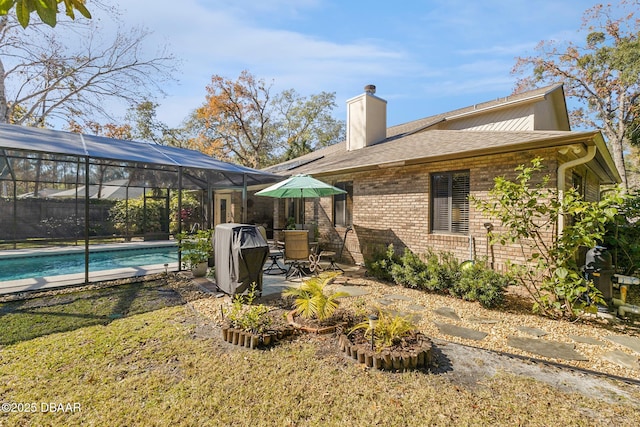 back of property with glass enclosure, brick siding, an outdoor pool, a chimney, and a patio area