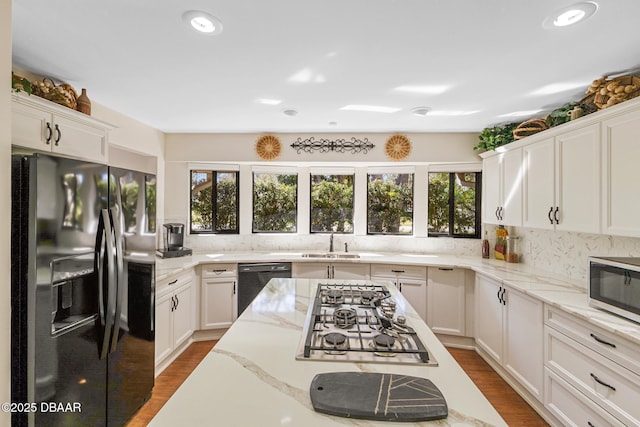 kitchen with decorative backsplash, wood finished floors, light stone countertops, black appliances, and a sink