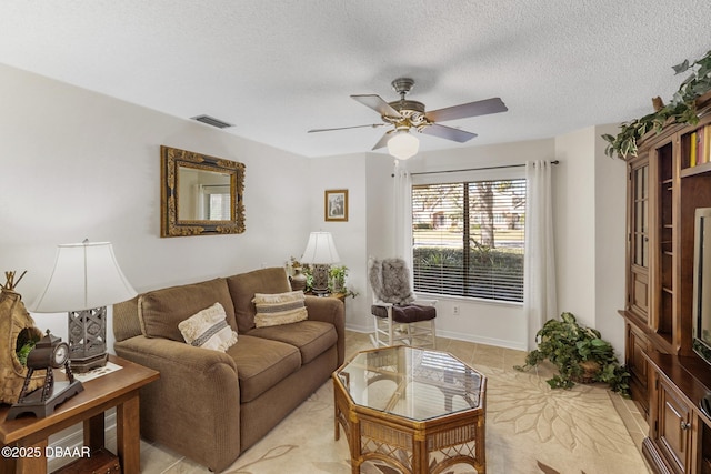 living area with baseboards, ceiling fan, visible vents, and a textured ceiling