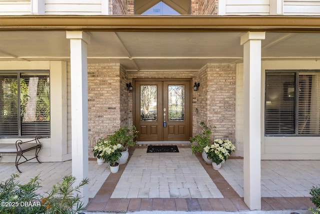 doorway to property featuring french doors, a porch, and brick siding