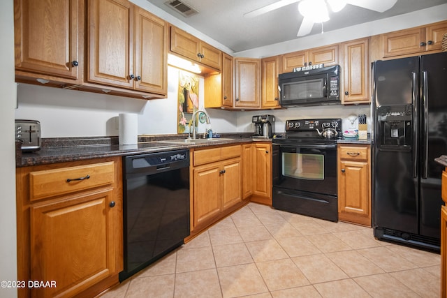 kitchen featuring dark stone counters, black appliances, sink, ceiling fan, and light tile patterned flooring