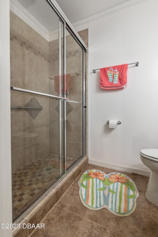 bathroom with tile patterned floors, toilet, a shower with door, and crown molding