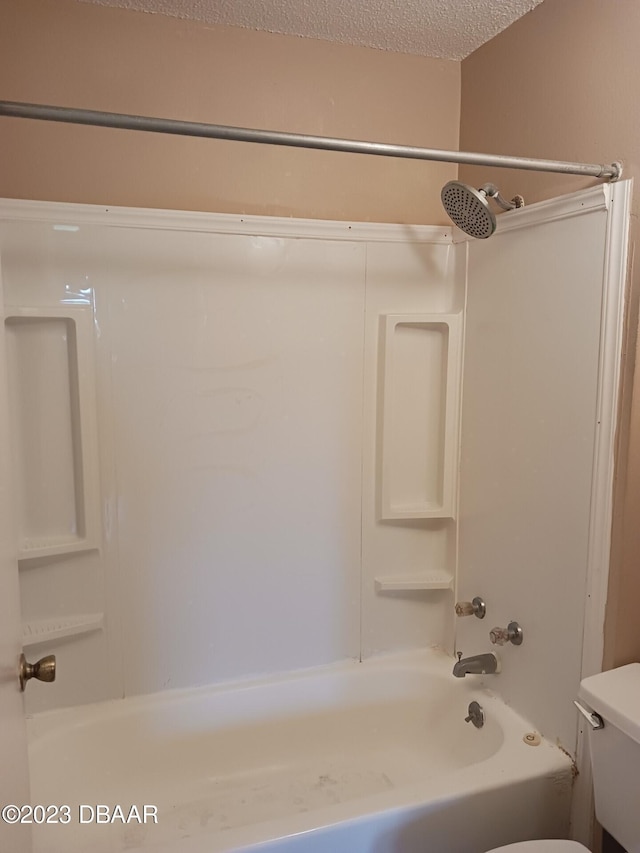 bathroom with a textured ceiling, toilet, and shower / bath combination