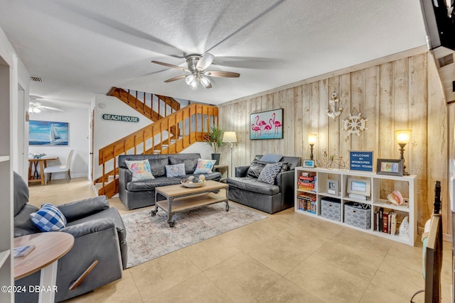 living room featuring ceiling fan, tile patterned floors, a textured ceiling, and wood walls