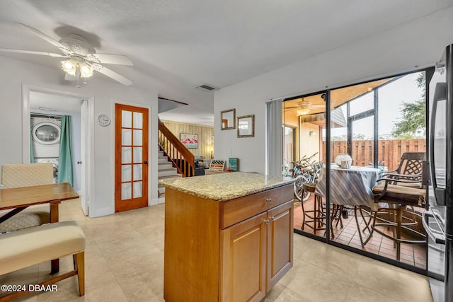 kitchen featuring a center island, stainless steel fridge, ceiling fan, stacked washer / dryer, and light stone countertops