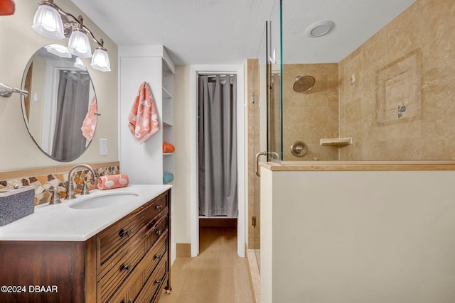 bathroom with tiled shower, vanity, wood-type flooring, and a textured ceiling