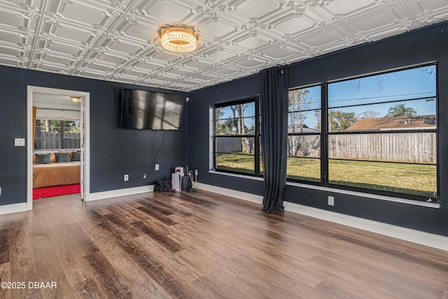 empty room with wood finished floors, an ornate ceiling, and baseboards