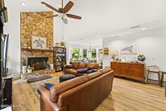 living room with a fireplace, light hardwood / wood-style floors, a high ceiling, and ceiling fan with notable chandelier