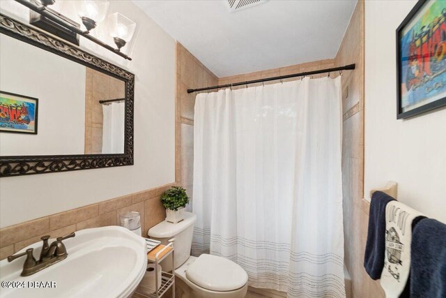 bathroom featuring tile walls, curtained shower, sink, and toilet