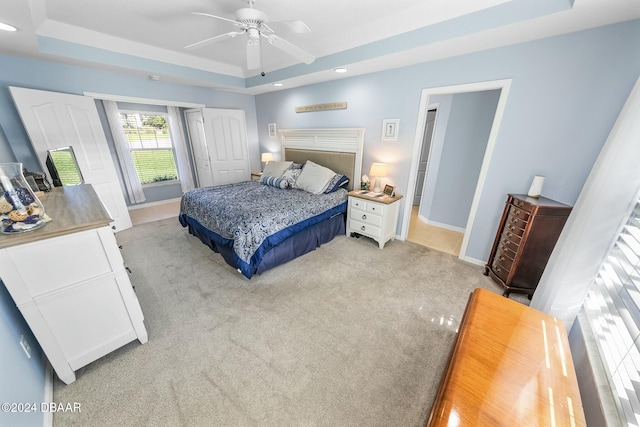 bedroom with light carpet, a closet, a tray ceiling, and ceiling fan