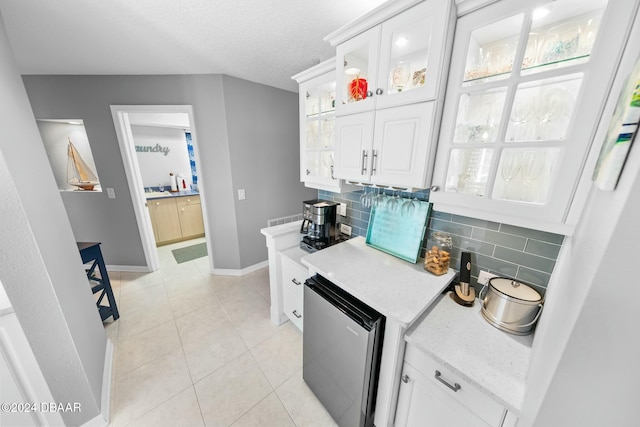 kitchen with white cabinets, backsplash, stainless steel refrigerator, and light tile patterned flooring