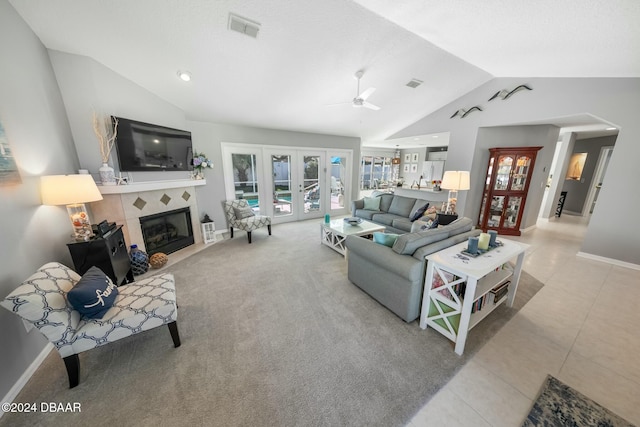 tiled living room with french doors, ceiling fan, lofted ceiling, and a tiled fireplace