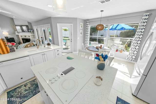 interior space featuring white appliances, sink, pendant lighting, white cabinets, and a tiled fireplace