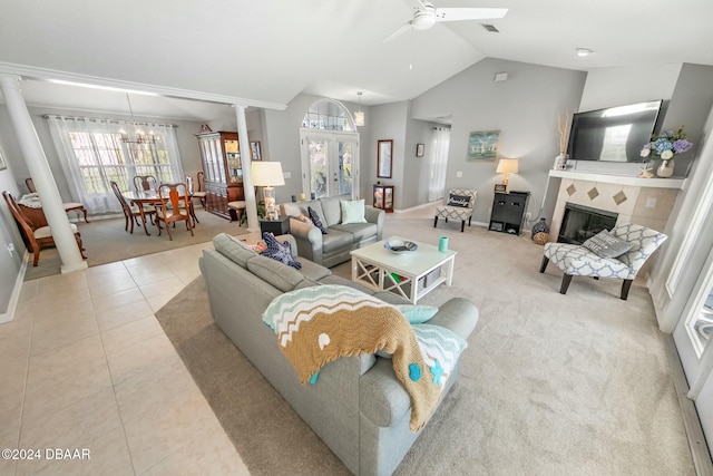 tiled living room featuring decorative columns, a tile fireplace, ceiling fan with notable chandelier, and vaulted ceiling