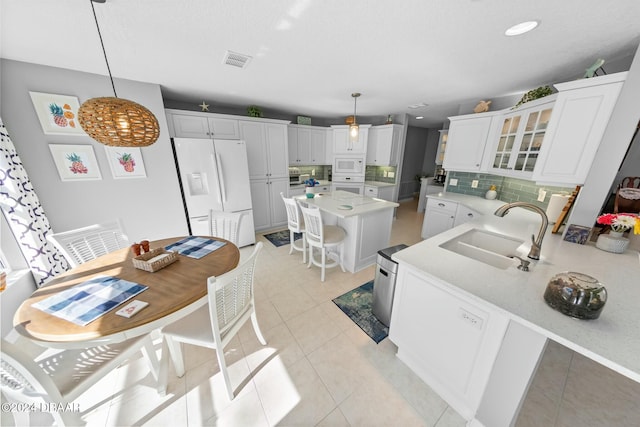 kitchen with decorative backsplash, white appliances, sink, pendant lighting, and white cabinetry