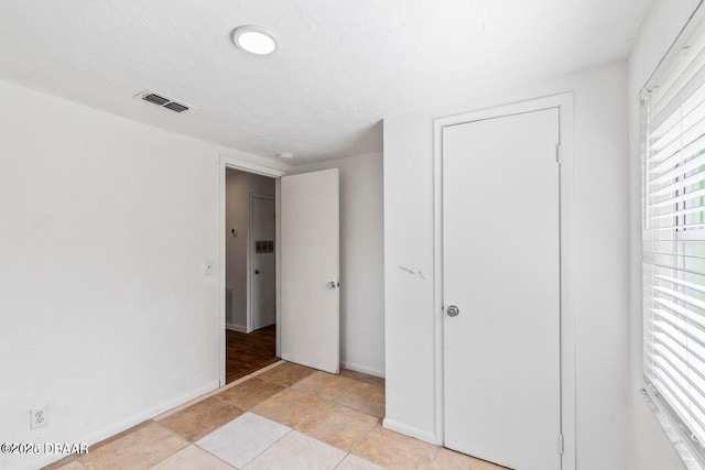 unfurnished bedroom featuring light tile patterned floors, baseboards, visible vents, and a closet