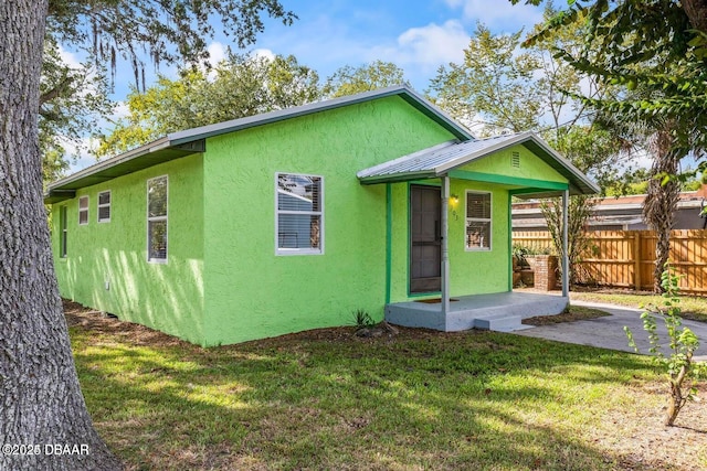 view of front of home featuring a front lawn, fence, stucco siding, metal roof, and a patio