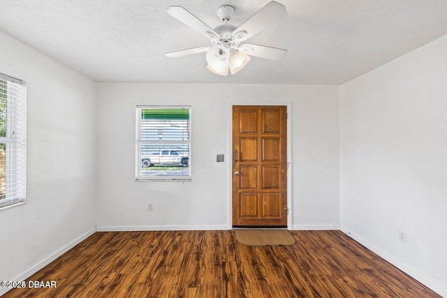 spare room with a healthy amount of sunlight, a textured ceiling, baseboards, and dark wood-style flooring