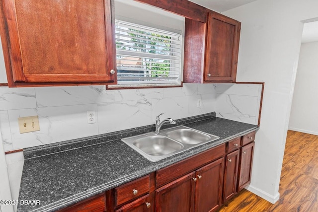 kitchen featuring a sink, baseboards, backsplash, and wood finished floors