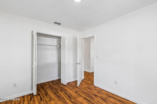 unfurnished bedroom with visible vents, wood finished floors, a closet, and baseboards