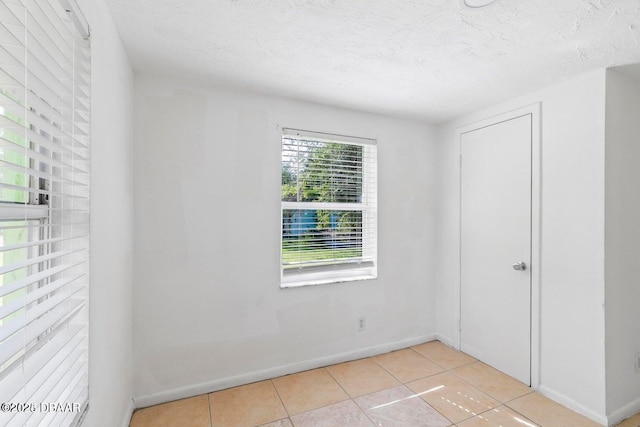 empty room featuring tile patterned floors, baseboards, and a textured ceiling