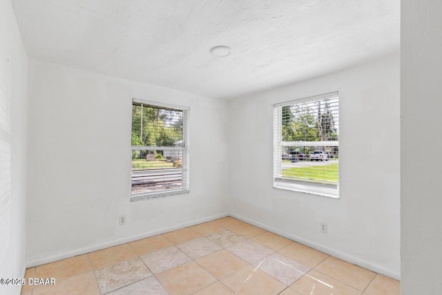 spare room featuring baseboards, a textured ceiling, and light tile patterned flooring