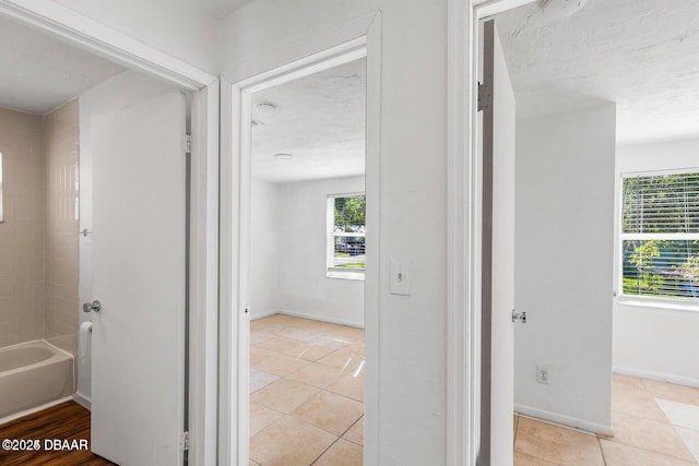 corridor with light tile patterned floors, baseboards, and a textured ceiling