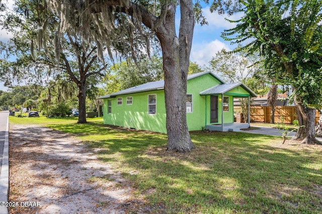 back of house with stucco siding, a lawn, metal roof, and fence